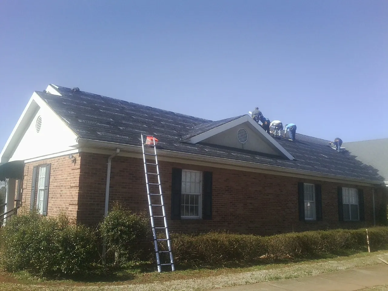 Crew tearing shingles off a brick ranch roof with a ladder set — Emergency Roof Repair work by our crew in Holmes