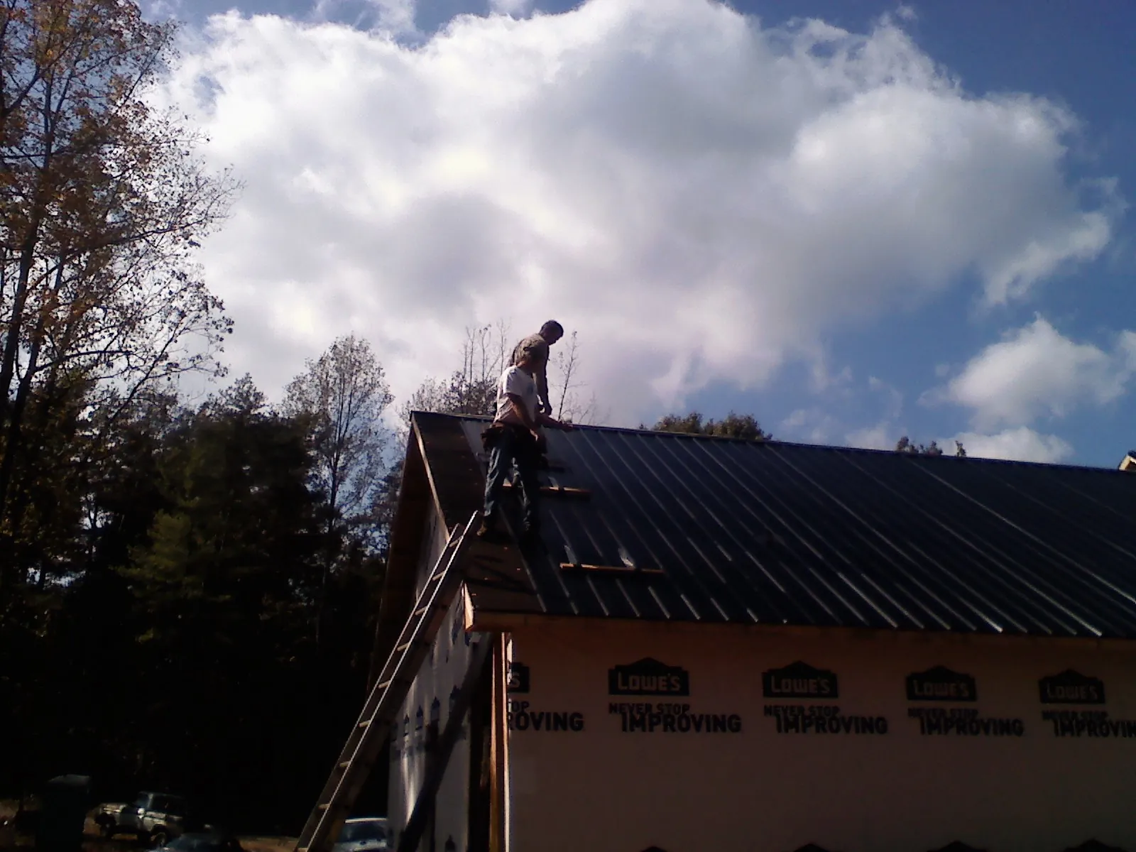 Roofer fastening dark metal panels high against a cloudy sky, from a Roof Inspection job in Holmes